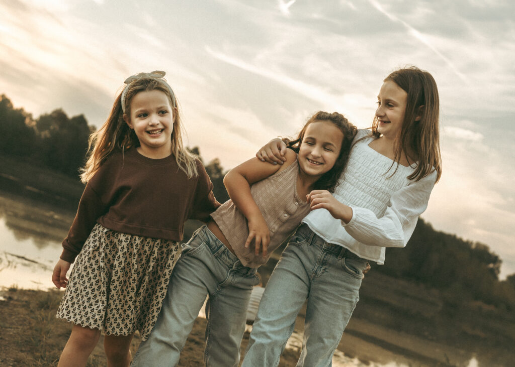 Candid moment of sisters laughing together at sunset by the water with a Cincinnati family photographer