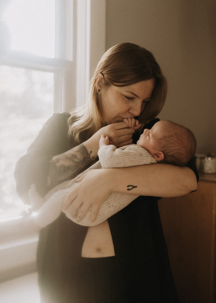mom kissing newborn baby's hand during in home lifestyle session in cincinnati
