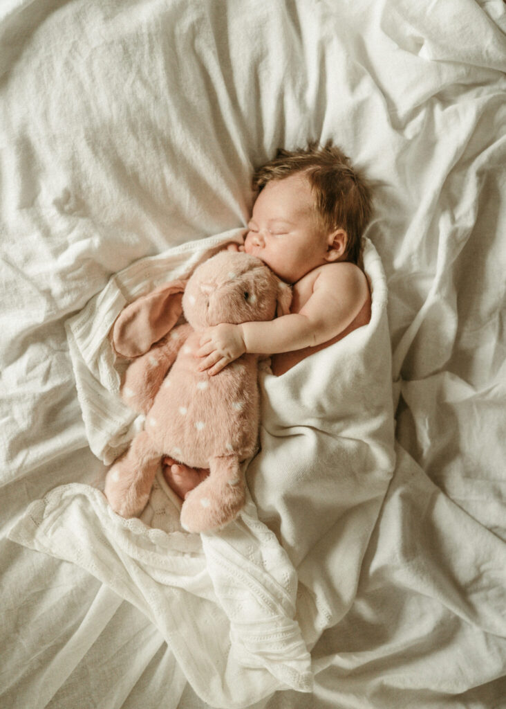 newborn baby in a white sheet sleeping and snuggling a pink bunny stuffed animal