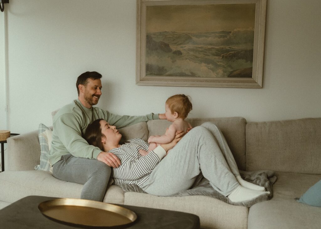 mom, dad, and toddler boy relaxing on their couch in a neutral living room during their lifestyle photography session in their cincinnati home