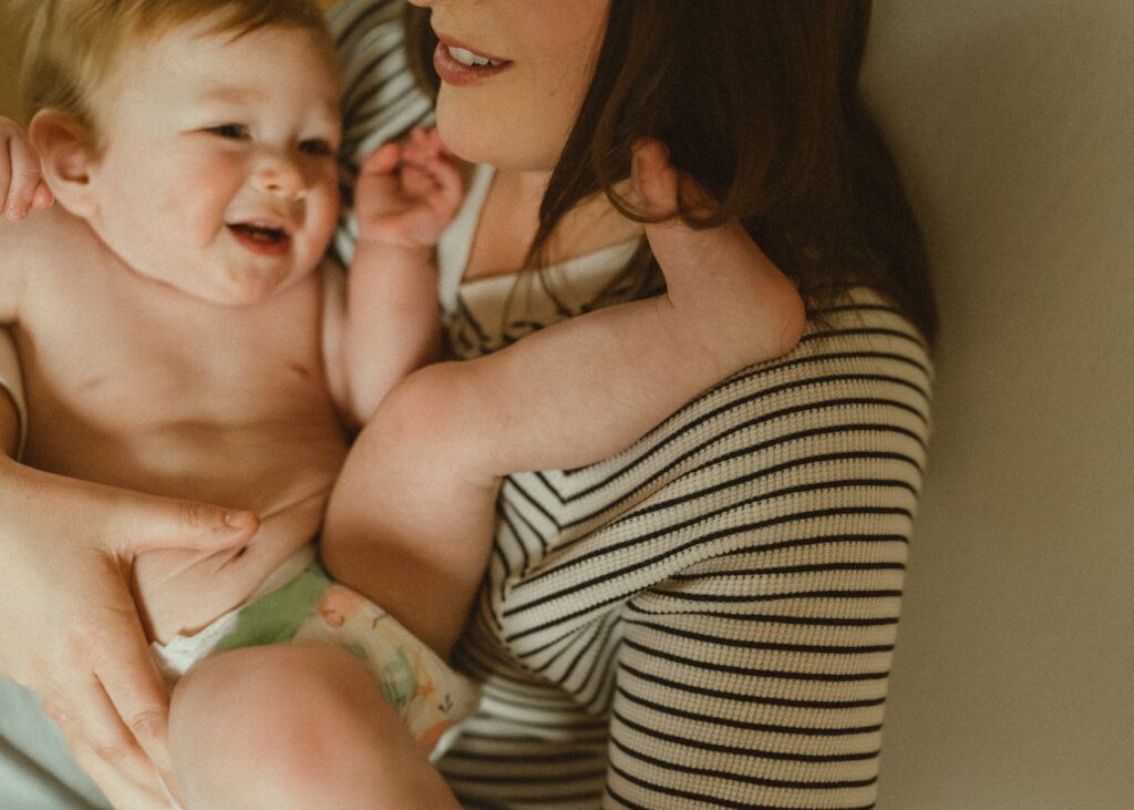 Toddler boy cuddling his mom while his foot gets wrapped in her hair during their photo session with a cincinnati lifestyle photographer in their home