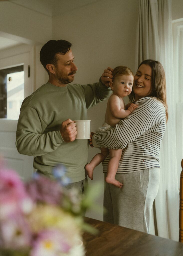 Dad brushing toddler's hair away while drinking a cup of coffee.