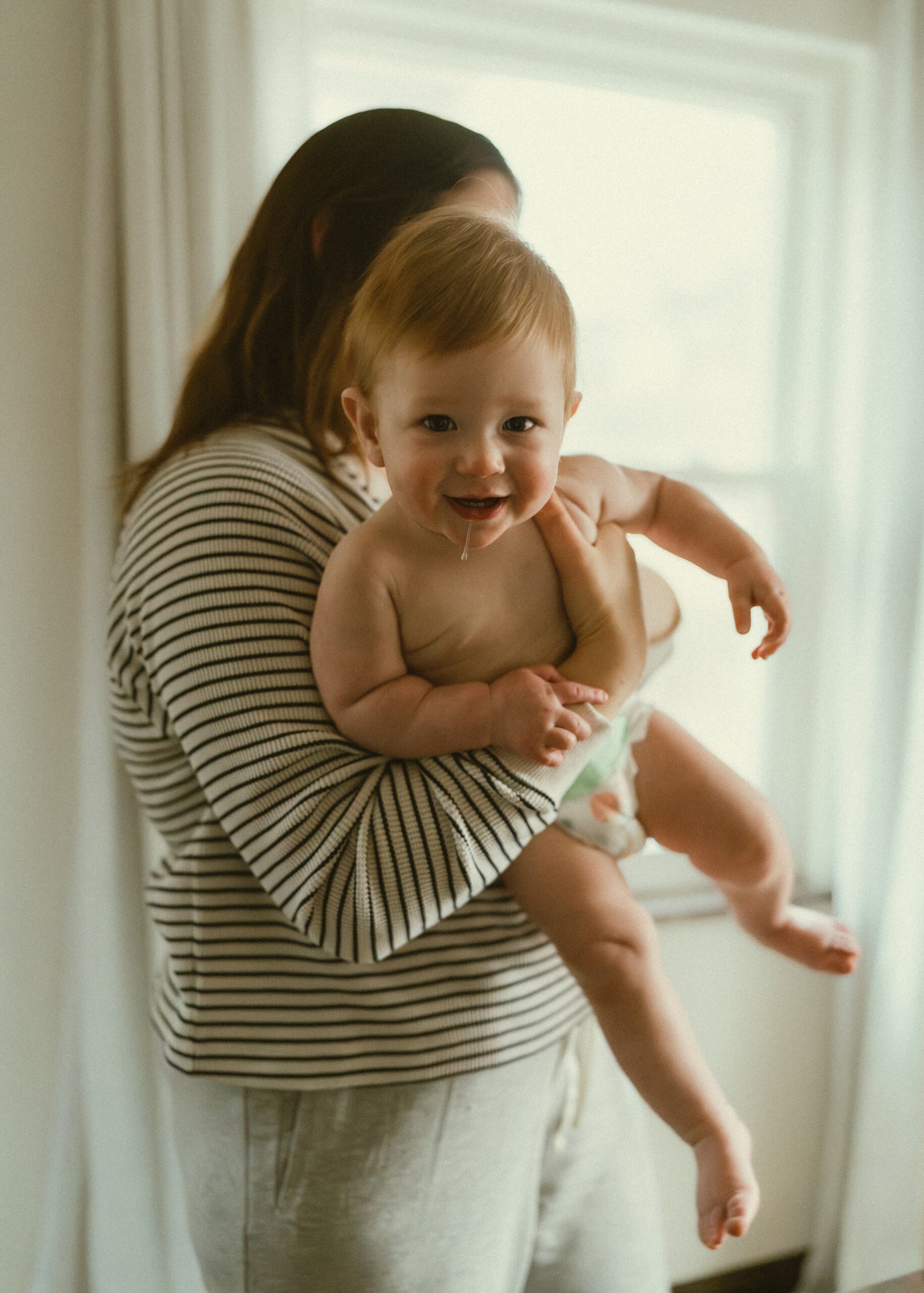 Toddler boy drooling while in his mom's arm smiling during their family lifestyle session in their cincinnati home.