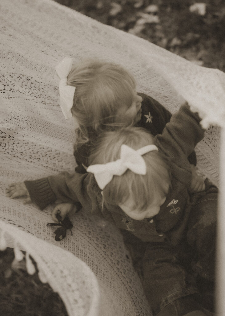 black and white photo of toddlers swinging in a lace blanket