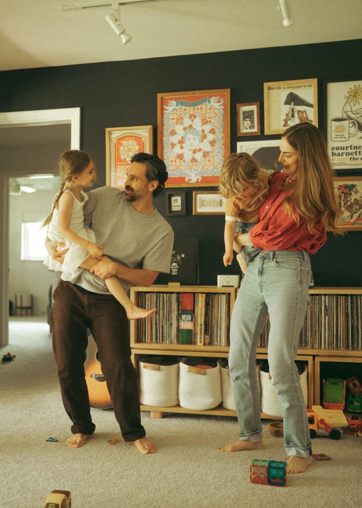 young family with two toddlers dancing in their living room with shelves of records and fun art behind them