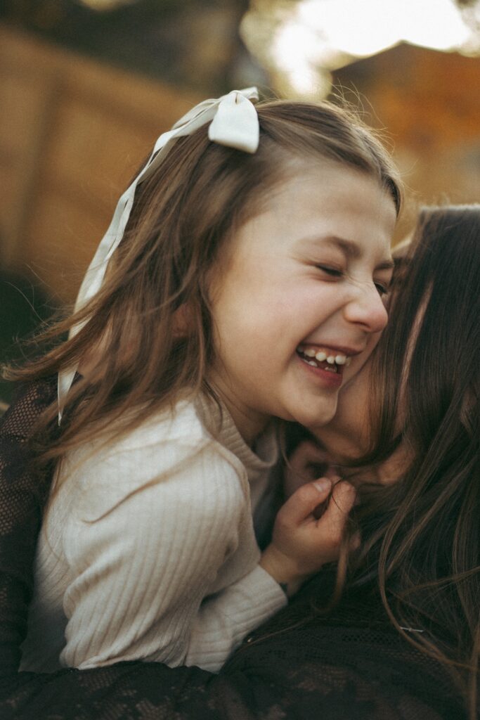closeup shot of little girl laughing with her eyes closed while mom kisses her cheek during their photography session in cincinnati