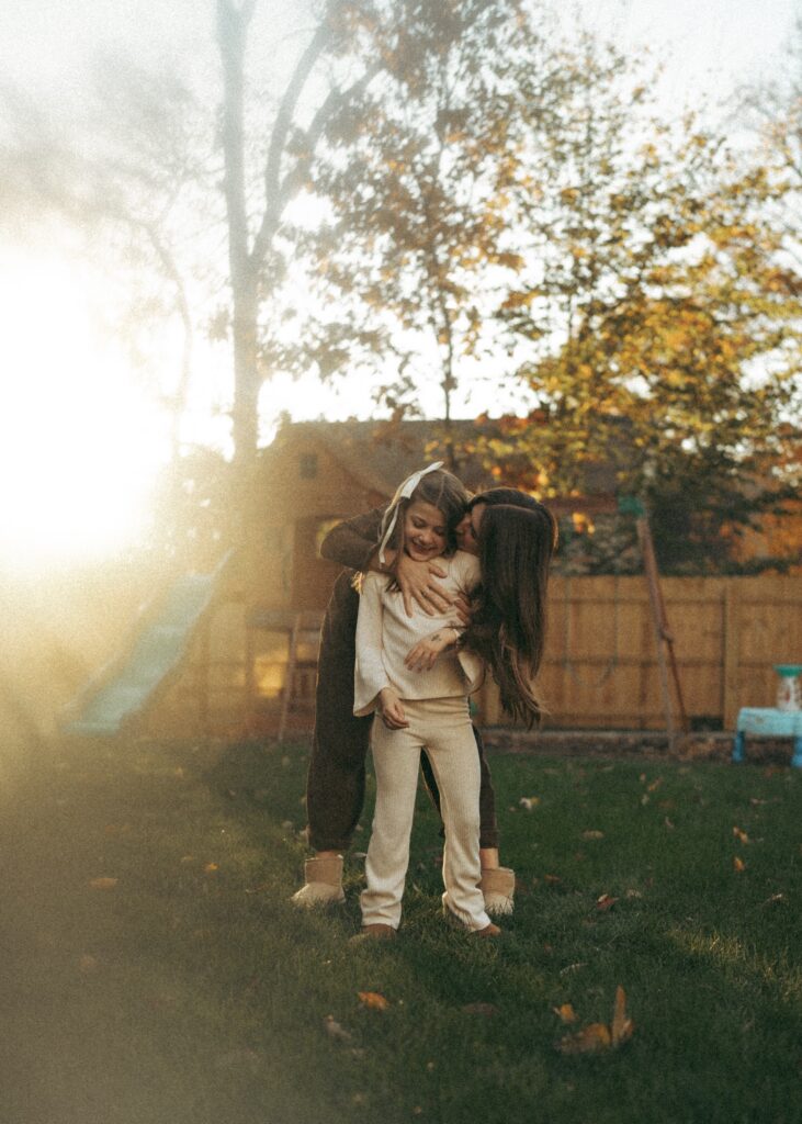 mom standing behind daughter giving her a hug with the sun setting behind them in their backyard during their lifestyle photographer session in cincinnati