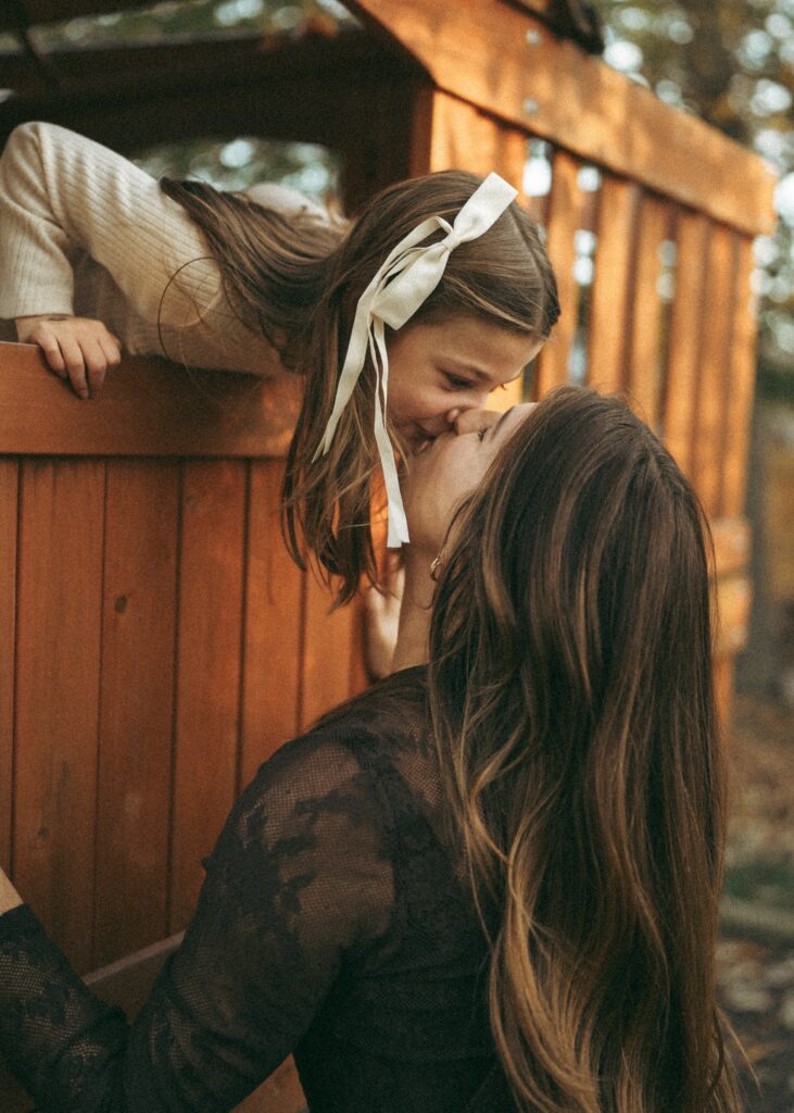 little girl standing in her playset leaning down to kiss mom