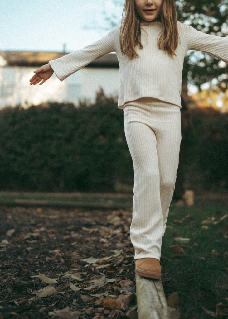 little girl balancing in her white outfit walking on a wooden beam