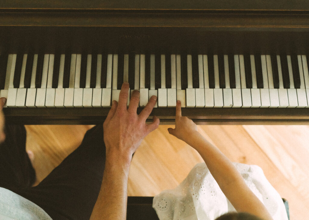toddler girl and her father's hands playing the piano 