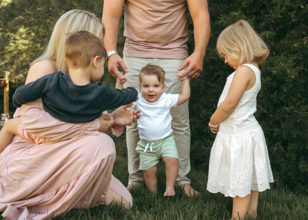 Cincinnati lifestyle photographer capturing family of 5 in their yard helping the youngest sibling walk