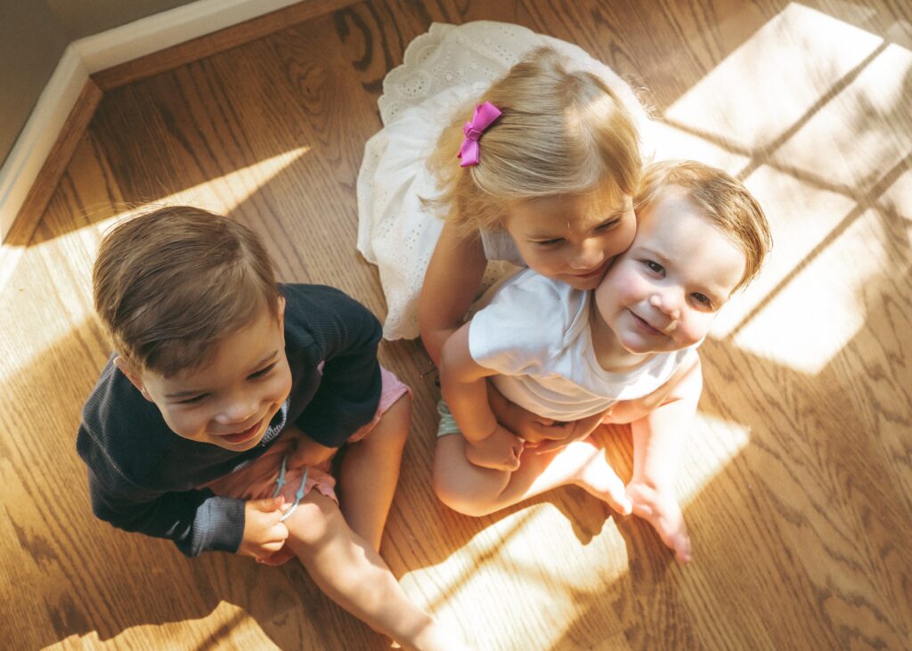 Three toddlers sitting in beautiful window light on their wood floor capture by Cincinnati lifestyle photographer