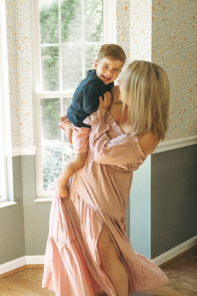 Cincinnati lifestyle photographer showcases mom in beautiful long pink dress holding her toddler son tickling him while he laughs