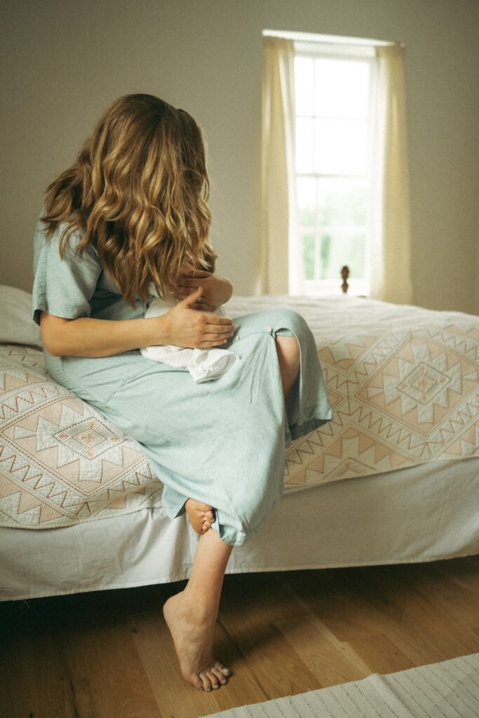 mom snuggling baby in denim dress on a bed during their cincinnati family photographer session