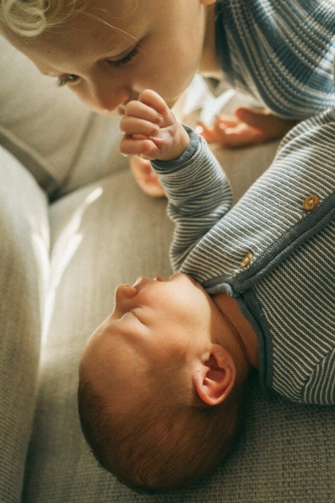 Lifestyle photo showing toddler playing with his newborn brother on the couch