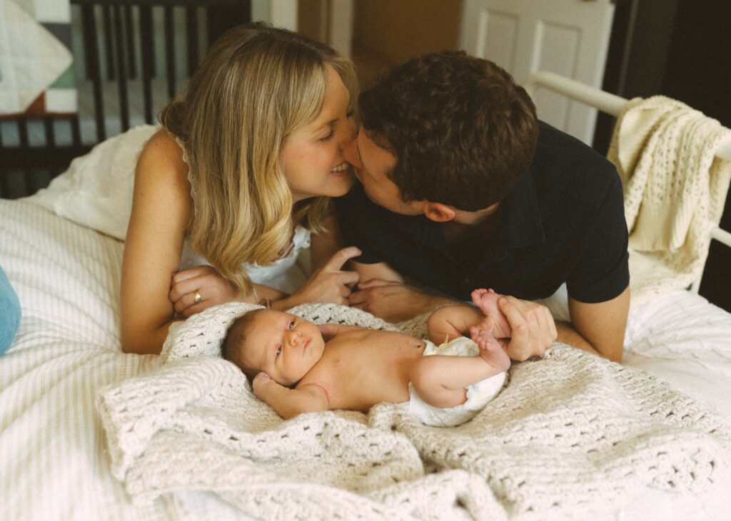mom and dad laughing while kissing with their newborn baby boy