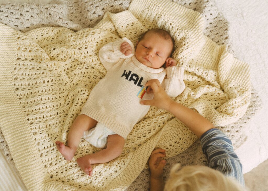 toddler brother putting a sticker on his newborn brother's white sweater