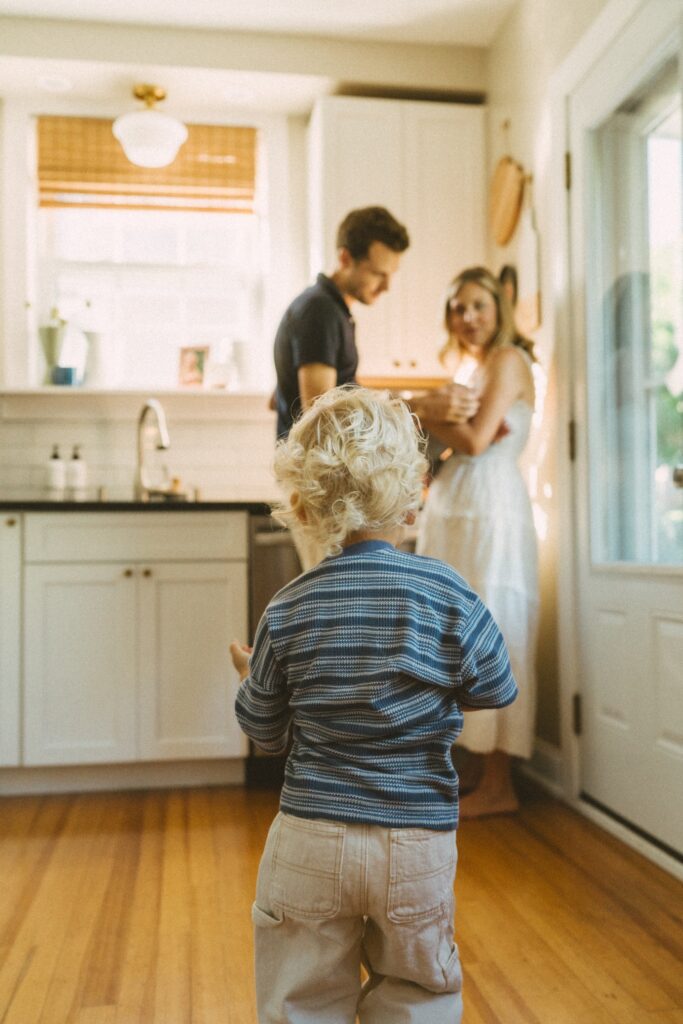 toddler boy running to his mom, dad, and newborn brother in their kitchen